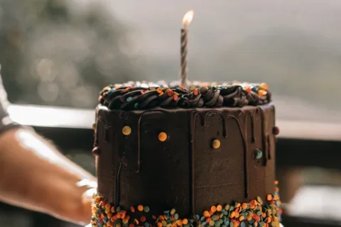 A person's hands hold up a small chocolate cake with a candle on it.