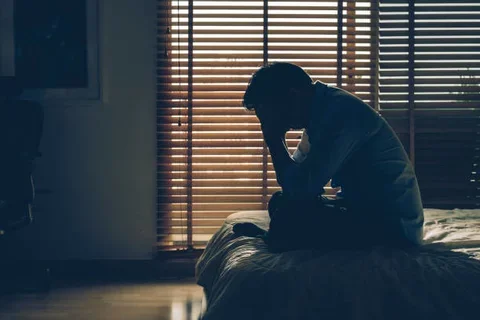 A depressed man sitting on a bed. 