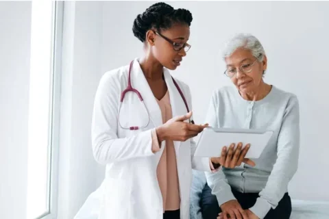 A Black female doctor shows a screen to an eldery Black patient.