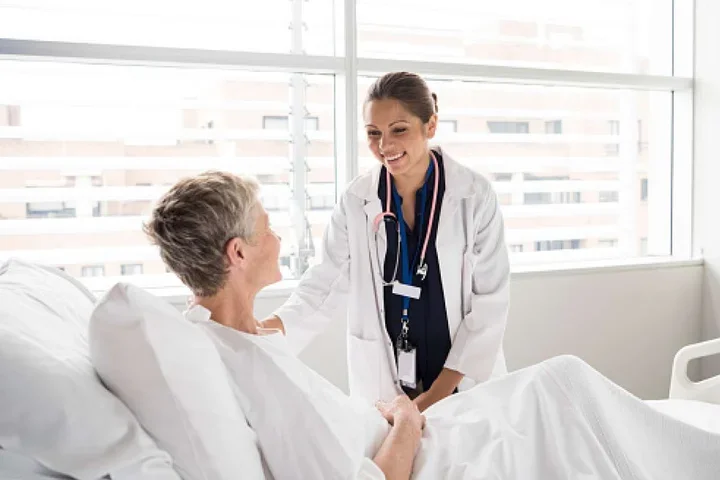 A female doctor smiles at an elderly patient in a hospital bed