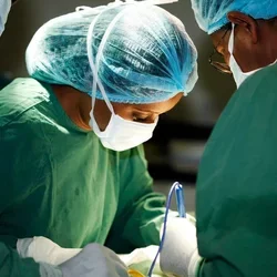 A group of surgeons operating on a patient with the spotlight on a Black female surgeon