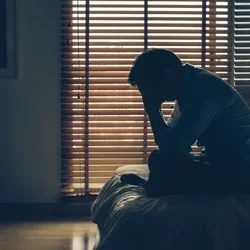 A depressed man sitting on a bed. 