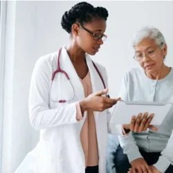 A Black female doctor shows a screen to an eldery Black patient. 