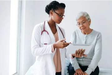 A Black female doctor shows a screen to an eldery Black patient. 
