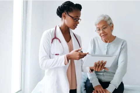 A Black female doctor shows a screen to an eldery Black patient.
